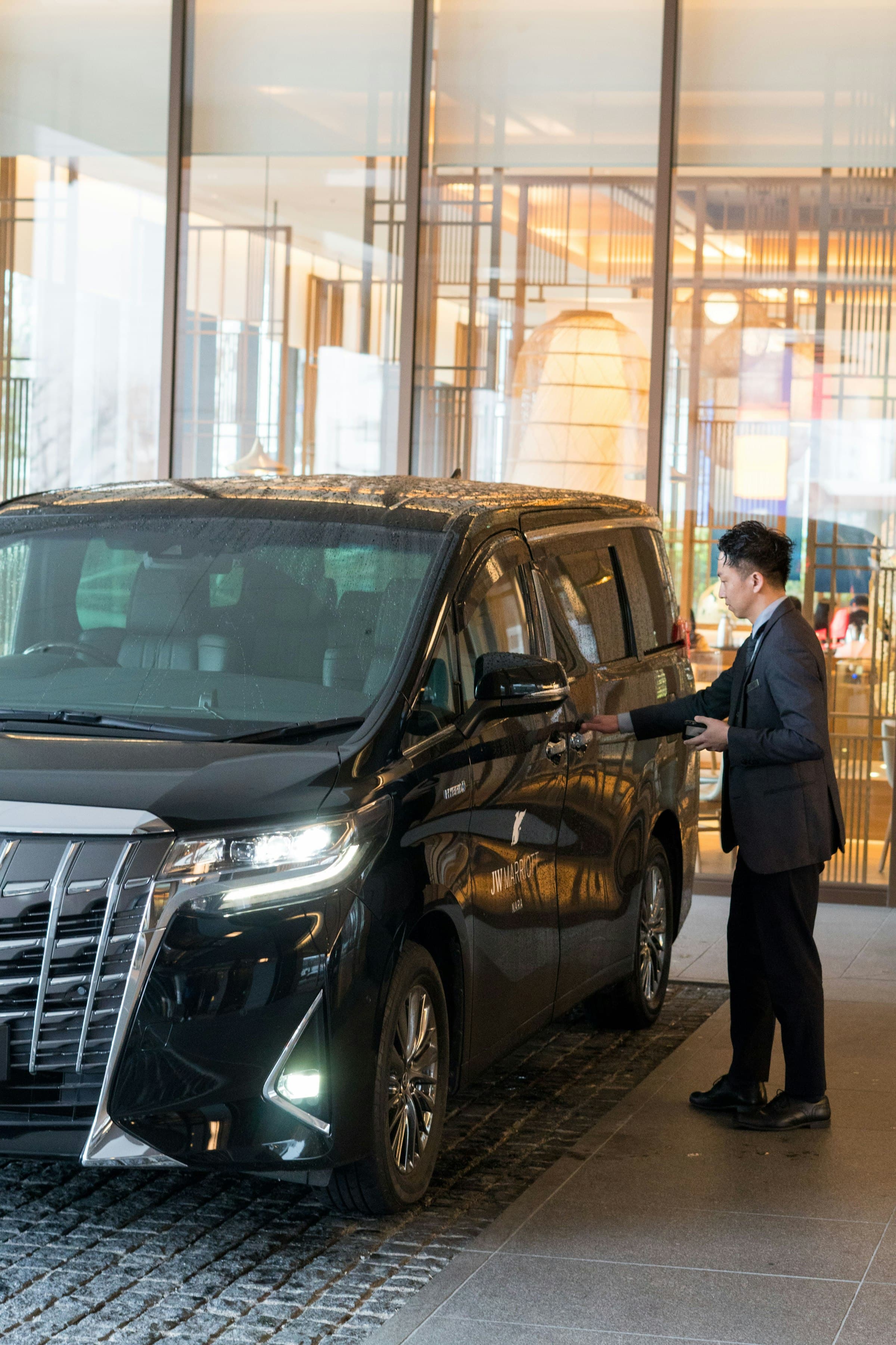 A chauffeur standing beside a black luxury car